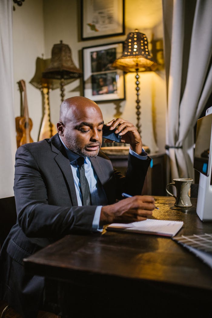 Businessman in a home office, taking notes during a phone call. Modern remote work setup.